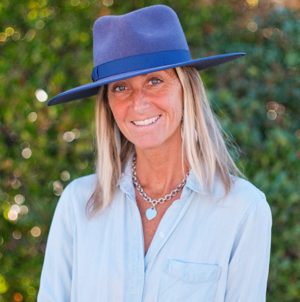 Portrait of a woman wearing a blue hat and a light blue shirt, smiling outdoors.