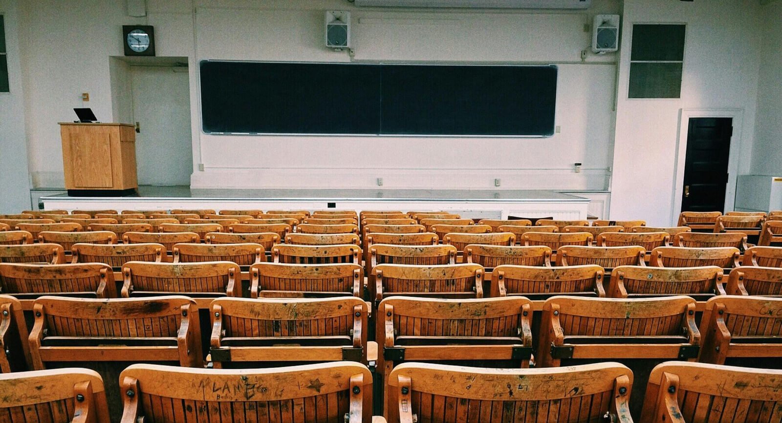 Empty lecture hall with wooden chairs facing a stage and podium, representing the setting for Walt's Cloud's inspiring speeches and professional presentations.